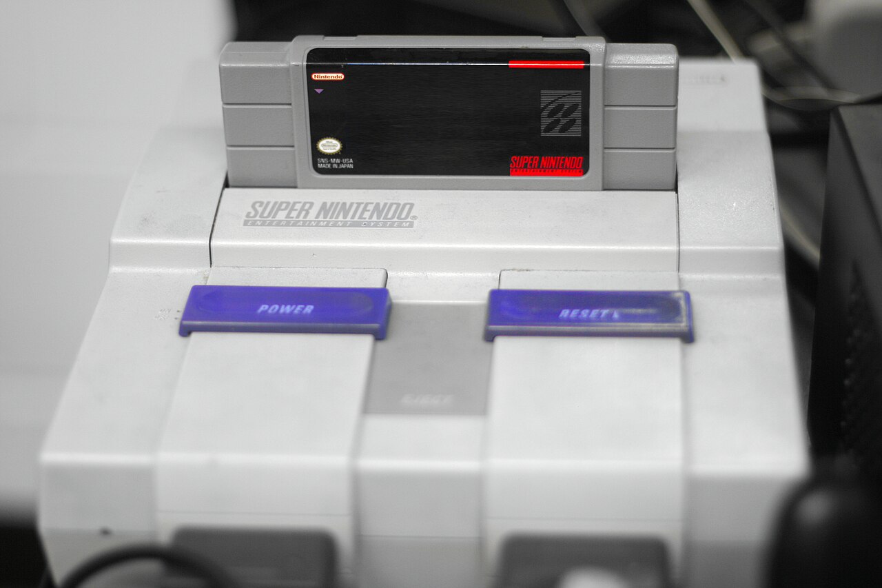 Super Mario World cartridge in a North American Super Nintendo, with the game artwork obscured in the source photograph